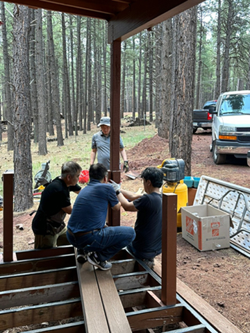 People gathered in a forest clearing with camping gear and a van nearby.