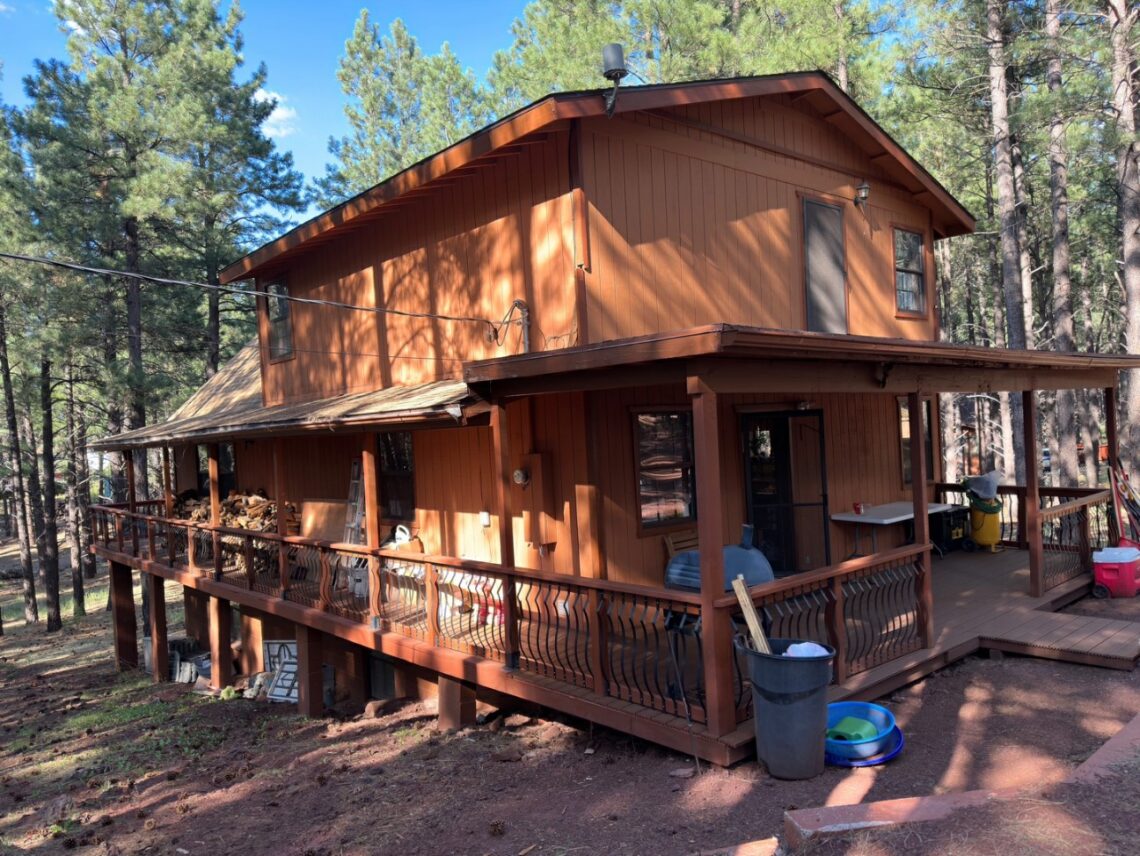 Cozy wooden cabin nestled in a forest with a wraparound porch.